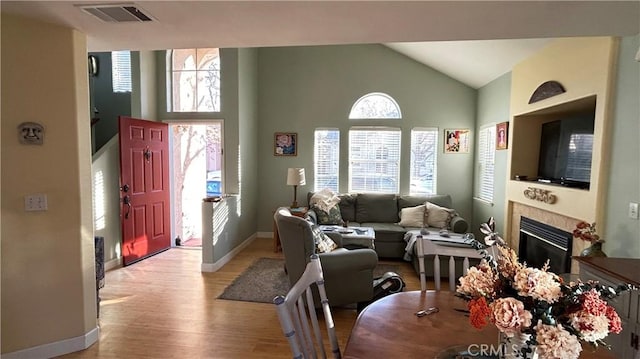 living room with visible vents, high vaulted ceiling, light wood-type flooring, baseboards, and a tile fireplace