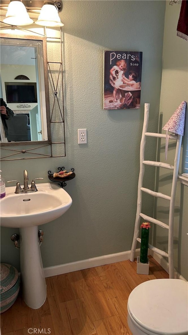 half bathroom featuring a textured wall, toilet, a sink, wood finished floors, and baseboards