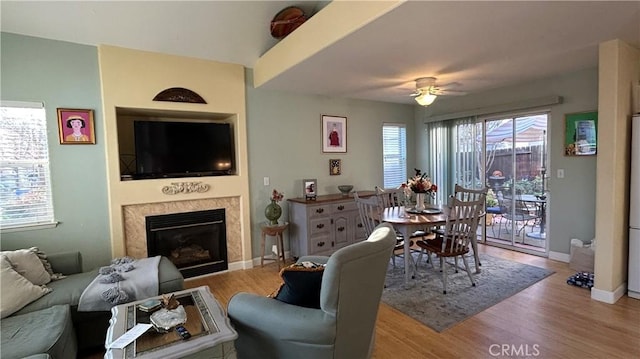 living area with light wood-type flooring, baseboards, a ceiling fan, and a high end fireplace