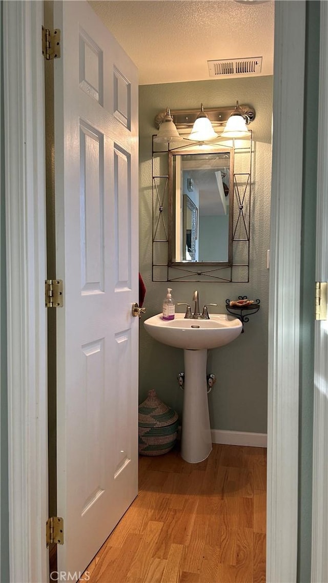 bathroom featuring visible vents, a sink, a textured ceiling, wood finished floors, and baseboards