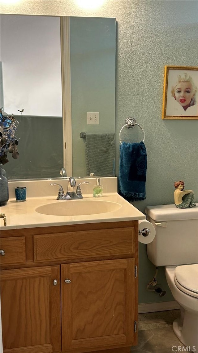 half bathroom with toilet, a textured wall, tile patterned flooring, and vanity