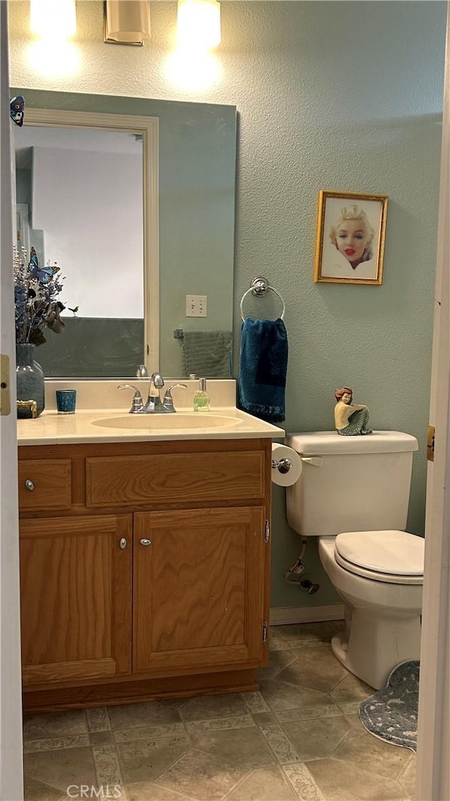 half bathroom with toilet, a textured wall, and vanity