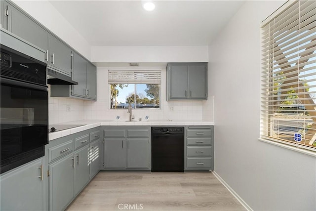 kitchen featuring black appliances, gray cabinetry, light wood-type flooring, and decorative backsplash