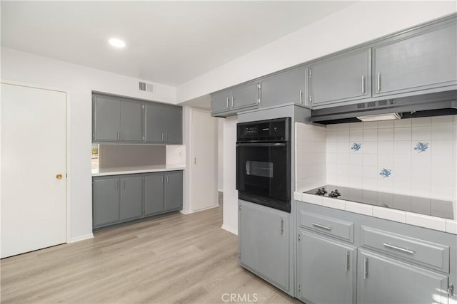 kitchen featuring tile countertops, black appliances, light wood-type flooring, gray cabinets, and backsplash