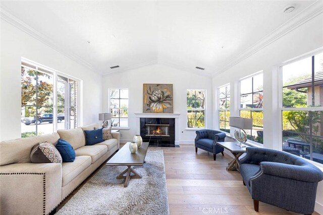 living area featuring crown molding, light wood finished floors, lofted ceiling, visible vents, and a fireplace with flush hearth