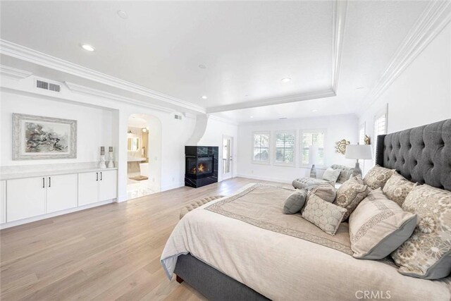 bedroom featuring visible vents, arched walkways, a glass covered fireplace, light wood-style floors, and recessed lighting