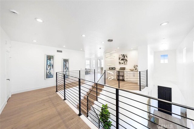 corridor with light wood-type flooring, baseboards, an upstairs landing, and recessed lighting