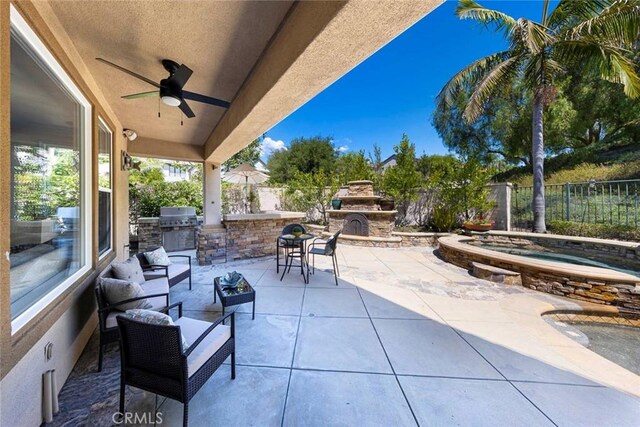 view of patio / terrace featuring an outdoor kitchen, a fenced backyard, an in ground hot tub, an outdoor stone fireplace, and a ceiling fan