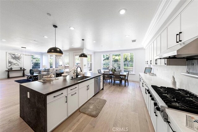 kitchen featuring white cabinets, an island with sink, dark countertops, stainless steel appliances, and a sink