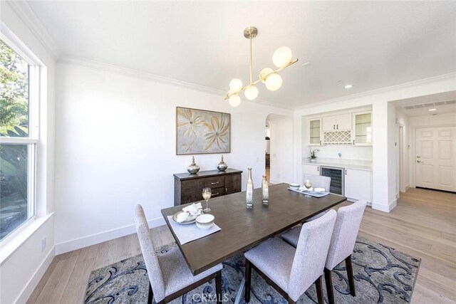 dining room featuring wine cooler, arched walkways, light wood-style flooring, ornamental molding, and baseboards