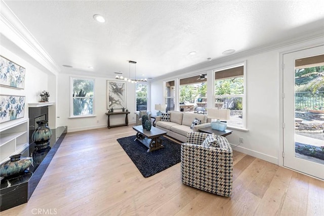 living area featuring a fireplace, crown molding, light wood finished floors, a textured ceiling, and baseboards