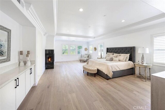 bedroom featuring recessed lighting, a lit fireplace, light wood finished floors, a raised ceiling, and crown molding