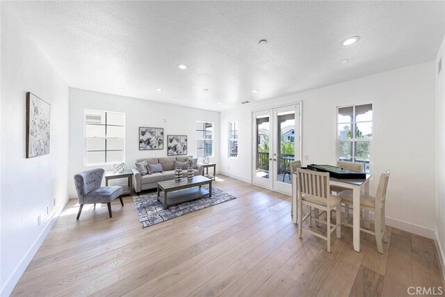 living room featuring light wood-style flooring, baseboards, a textured ceiling, and french doors