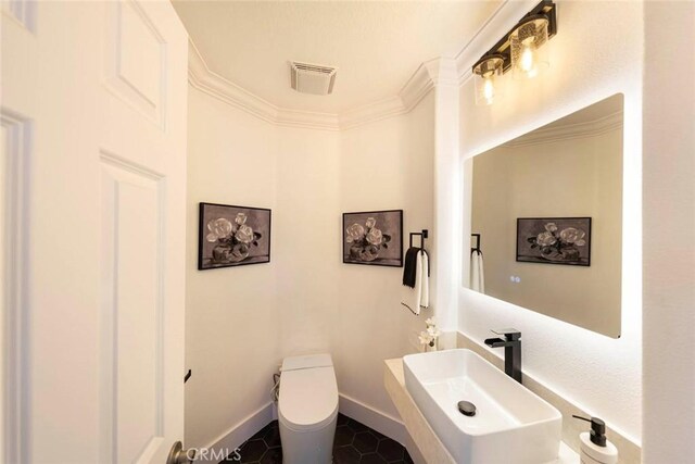 bathroom with toilet, a sink, visible vents, baseboards, and crown molding