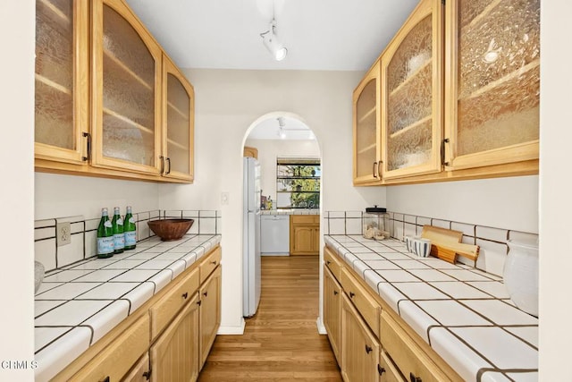 kitchen featuring white appliances, light wood-type flooring, light brown cabinets, and tile counters