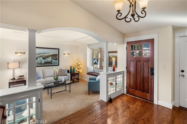 foyer entrance with dark wood-type flooring, ornate columns, a chandelier, and lofted ceiling