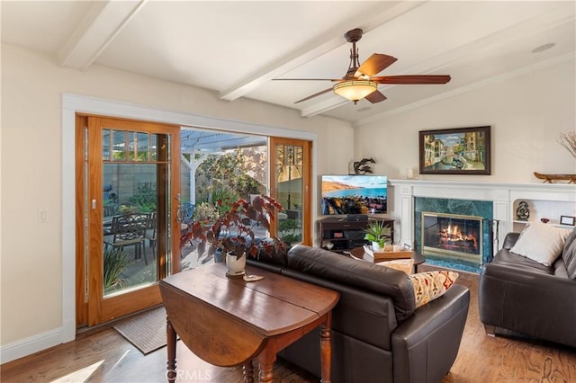 living room with a premium fireplace, ceiling fan, wood-type flooring, and lofted ceiling with beams