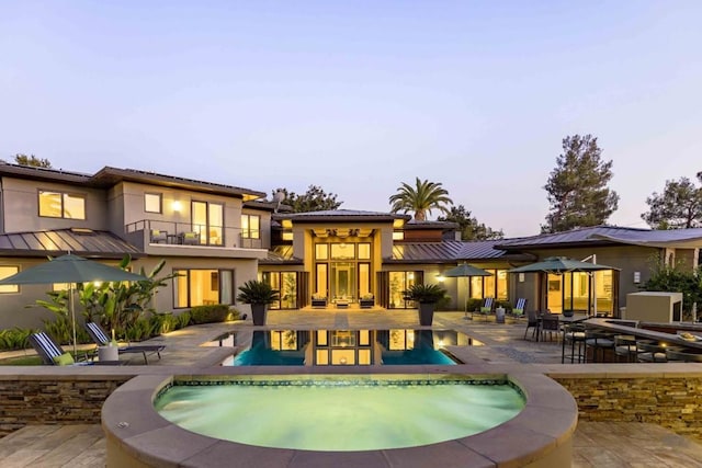 pool at dusk with a hot tub and a patio