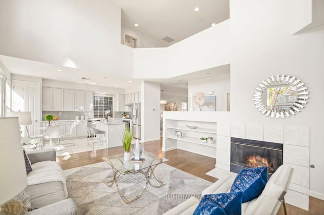 living room featuring a towering ceiling, a fireplace, and light hardwood / wood-style flooring