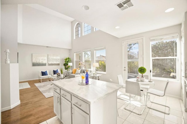 kitchen featuring a center island, light tile patterned floors, white cabinetry, and light stone countertops