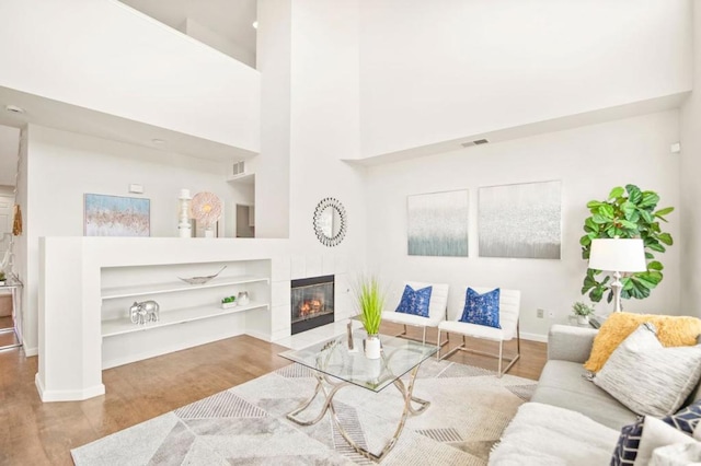 living room with a towering ceiling, a tiled fireplace, hardwood / wood-style floors, and built in shelves