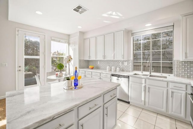 kitchen with stainless steel dishwasher, white cabinets, sink, and light stone countertops