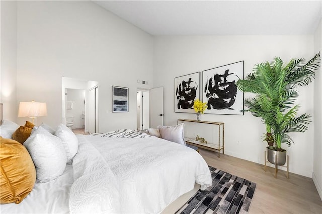 bedroom with light hardwood / wood-style flooring, ensuite bathroom, and high vaulted ceiling