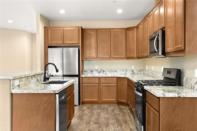 kitchen with light stone counters, stainless steel appliances, light hardwood / wood-style floors, and sink