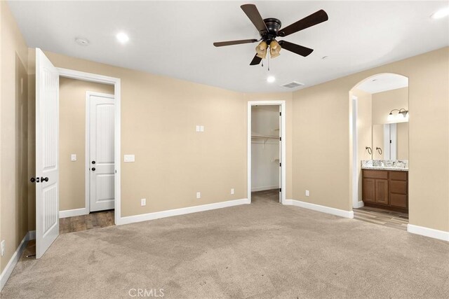 unfurnished bedroom featuring a closet, ensuite bath, light carpet, and ceiling fan