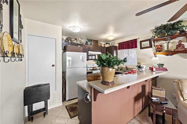 kitchen with white appliances, a kitchen breakfast bar, kitchen peninsula, ceiling fan, and light tile patterned floors