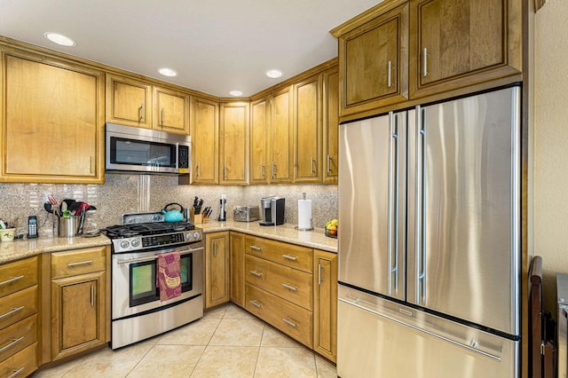 kitchen featuring light stone counters, appliances with stainless steel finishes, light tile patterned flooring, and tasteful backsplash