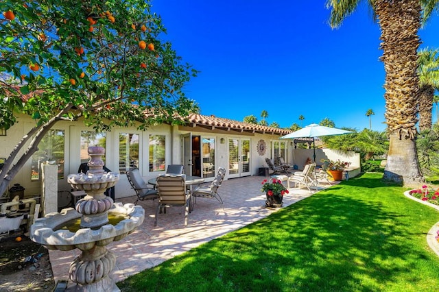 rear view of property featuring a lawn, french doors, and a patio area