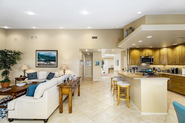 kitchen featuring light stone counters, tasteful backsplash, a breakfast bar area, appliances with stainless steel finishes, and light tile patterned flooring