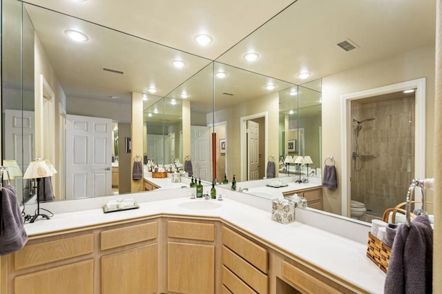 bathroom with toilet, tiled shower, and vanity