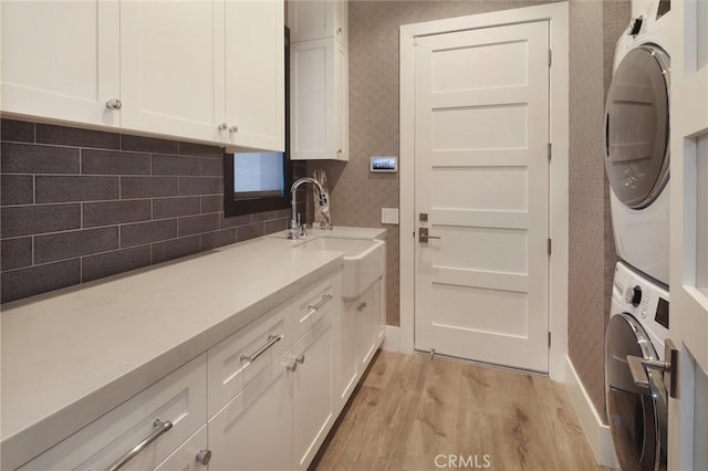 laundry room featuring cabinets, stacked washer and clothes dryer, sink, and light hardwood / wood-style floors