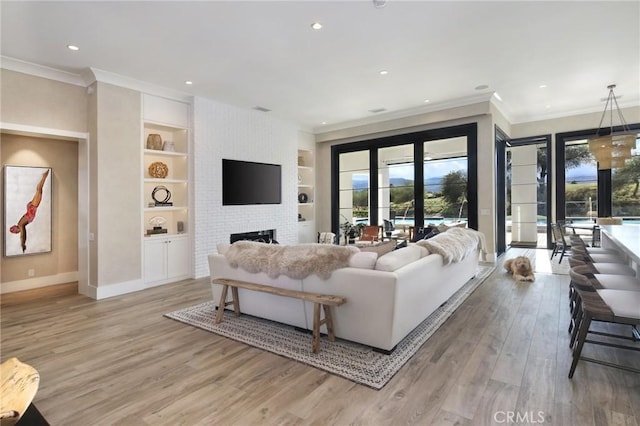 living room featuring ornamental molding, a brick fireplace, built in features, and light wood-type flooring