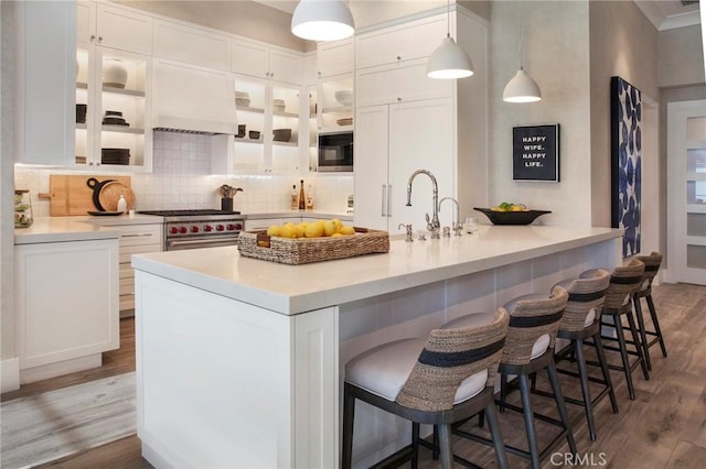 kitchen with sink, high end range, white cabinetry, a kitchen bar, and decorative light fixtures