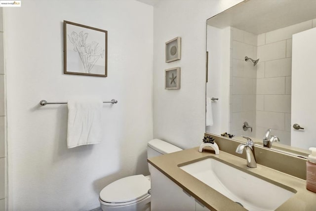 bathroom featuring a tile shower, vanity, and toilet