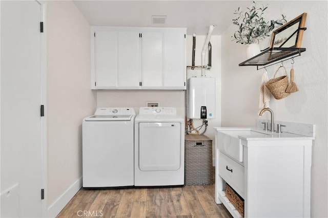 clothes washing area featuring water heater, washer and dryer, cabinets, and light wood-type flooring