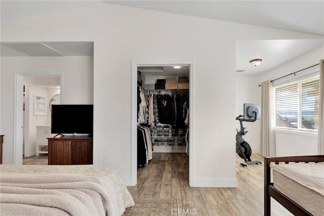 bedroom with a spacious closet, ensuite bathroom, a closet, light hardwood / wood-style floors, and lofted ceiling