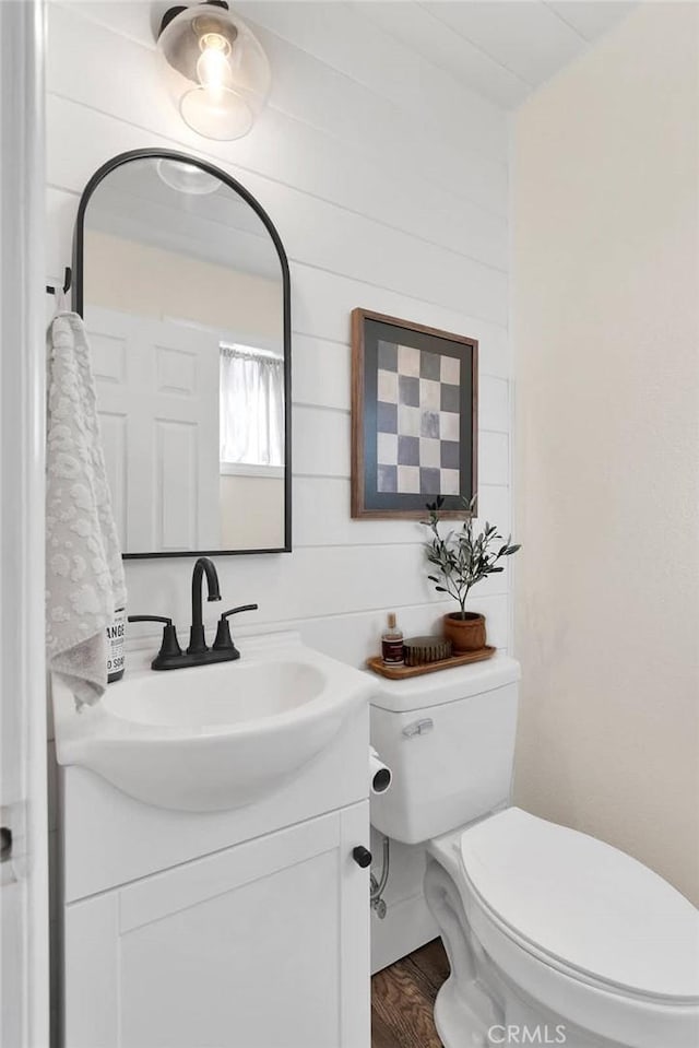 bathroom featuring wood walls, toilet, vanity, and hardwood / wood-style flooring