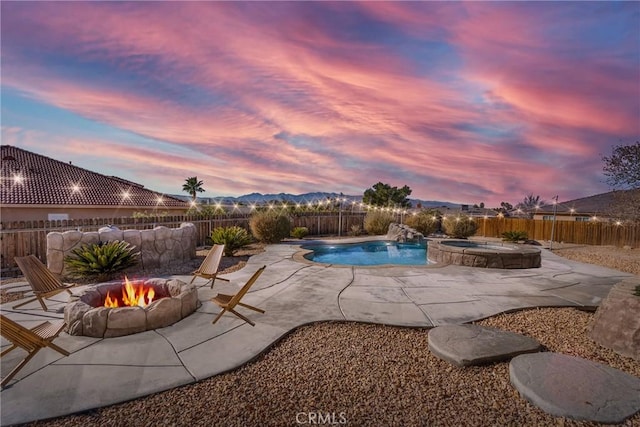 pool at dusk with an outdoor fire pit, a patio, pool water feature, and an in ground hot tub