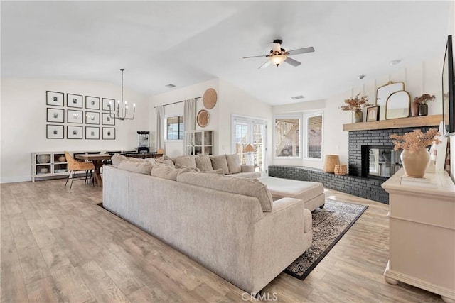 living room with ceiling fan with notable chandelier, light hardwood / wood-style flooring, lofted ceiling, and a fireplace