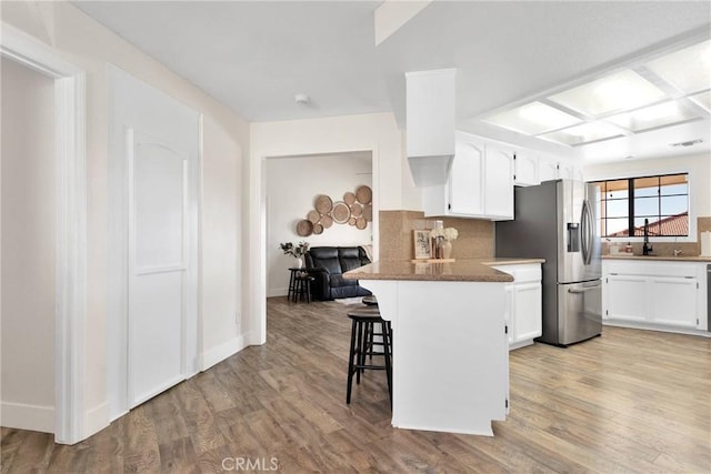 kitchen with white cabinets, a kitchen breakfast bar, kitchen peninsula, backsplash, and stainless steel fridge