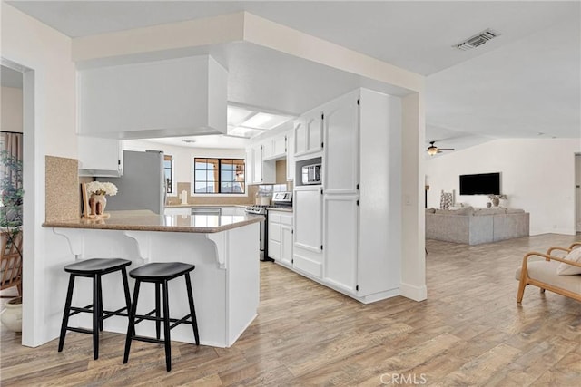 kitchen featuring appliances with stainless steel finishes, white cabinets, a kitchen bar, and kitchen peninsula