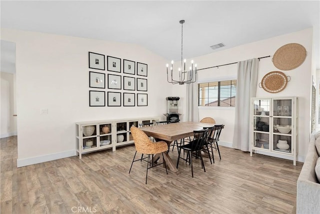 dining area with hardwood / wood-style flooring, an inviting chandelier, and vaulted ceiling