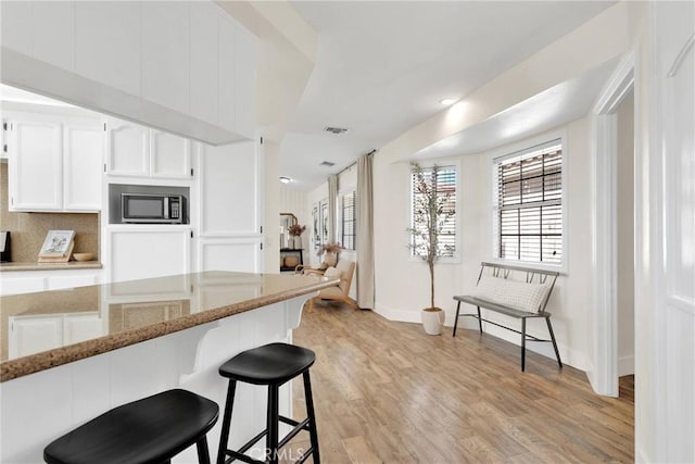 kitchen with light stone countertops, light hardwood / wood-style flooring, a breakfast bar, tasteful backsplash, and white cabinets