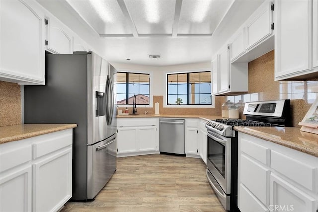 kitchen featuring white cabinetry, stainless steel appliances, decorative backsplash, sink, and light hardwood / wood-style flooring