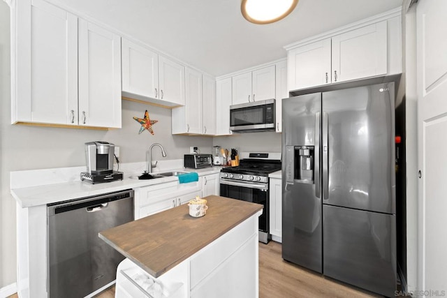 kitchen with stainless steel appliances, sink, white cabinetry, a center island, and light wood-type flooring