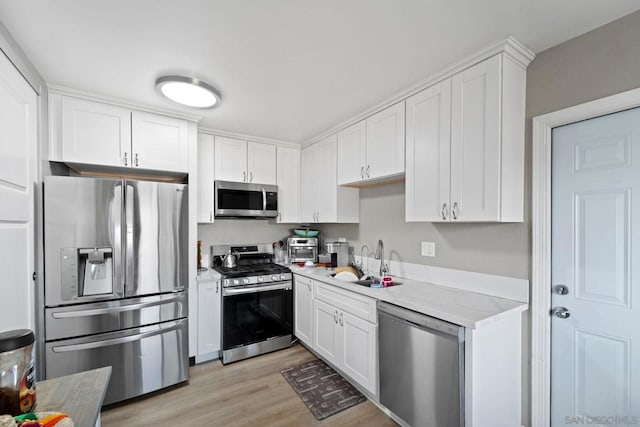 kitchen with stainless steel appliances, light stone countertops, sink, light hardwood / wood-style flooring, and white cabinetry